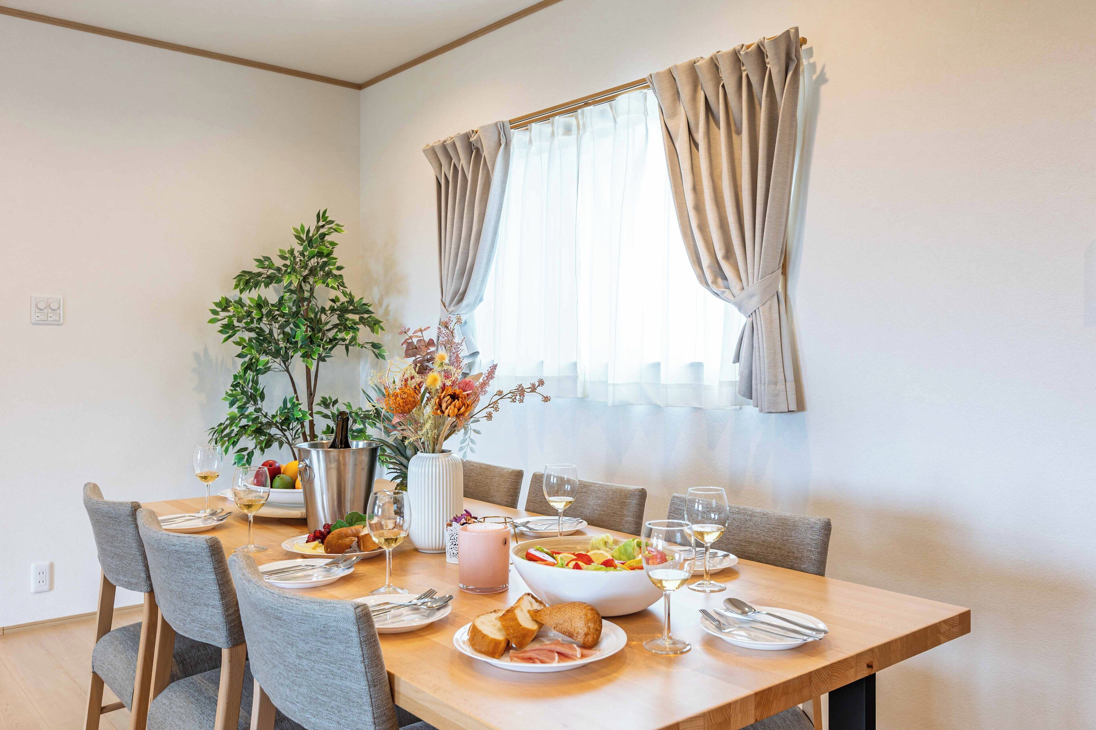 Un coin repas avec une table en bois dressée pour quatre personnes, entourée de chaises grises. Un vase avec des fleurs et un panier de fruits sont posés sur la table.