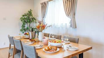Un coin repas avec une table en bois dressée pour quatre personnes, entourée de chaises grises. Un vase avec des fleurs et un panier de fruits sont posés sur la table.