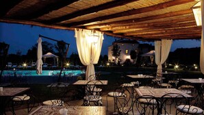 Un espace extérieur aménagé pour les repas, avec des tables et des chaises, une piscine et un bâtiment en arrière-plan.