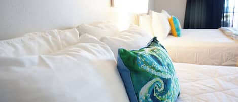 Habitación de hotel con dos camas, ropa de cama blanca y un cojín estampado en verde.