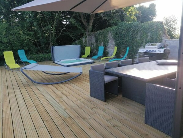 Eine Holzterrasse mit Gartenmöbeln, darunter Stühle, ein Tisch und ein Grill.