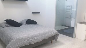 A bedroom with a bed, two pillows, a bedside table, a wardrobe, and a glass shower enclosure.