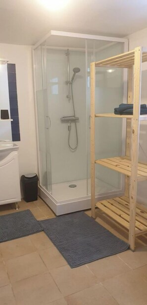 Ein modernes Badezimmer mit einer gläsernen Duschkabine, einem weißen Waschbecken und einer Holzregaleinrichtung.
