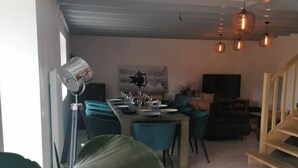 A modern dining area with a long table set for four, a ceiling fan, and a staircase to the right.