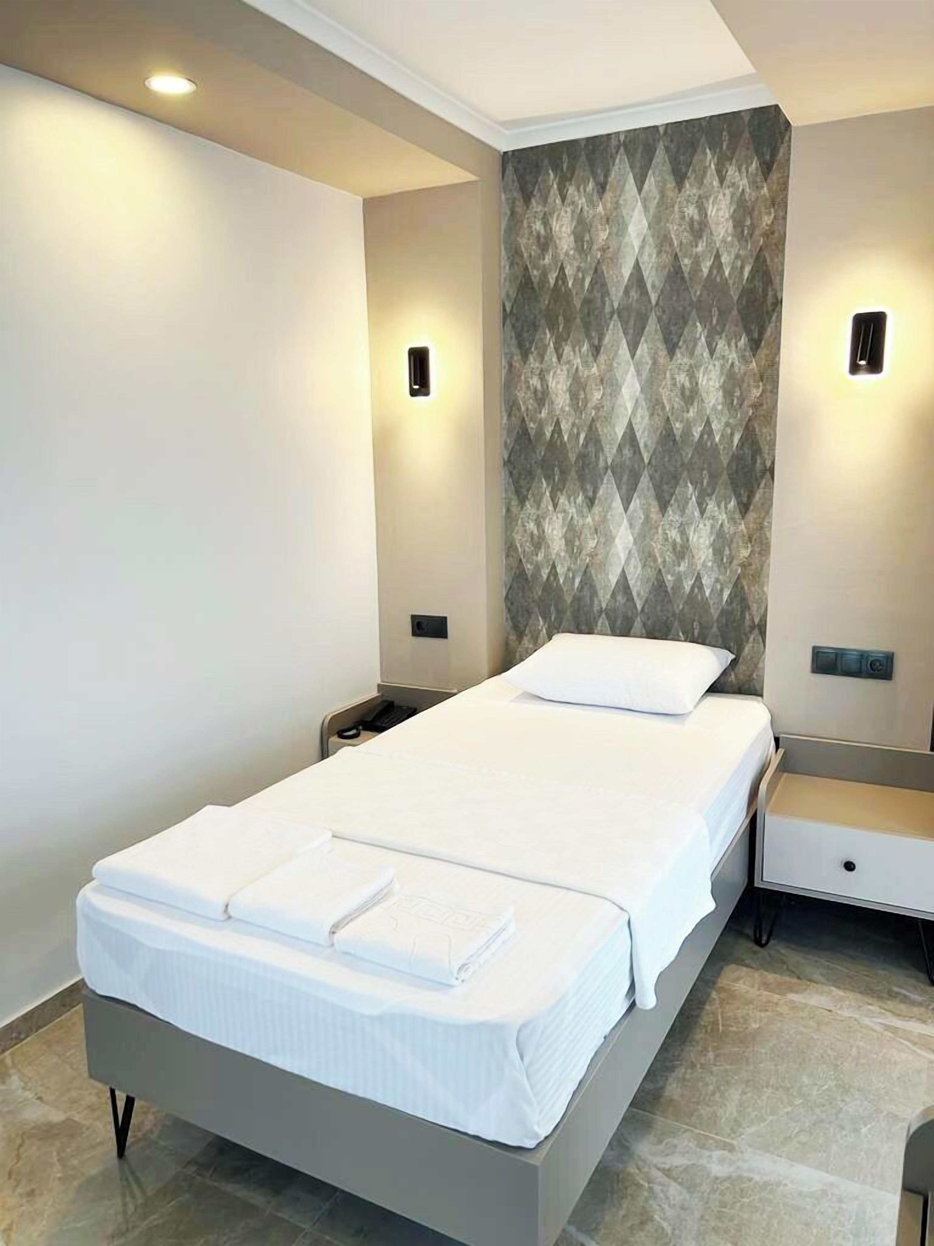 Habitación de hotel moderna con una cama grande, una mesita de noche, una lámpara de pared y una pared con estampado.