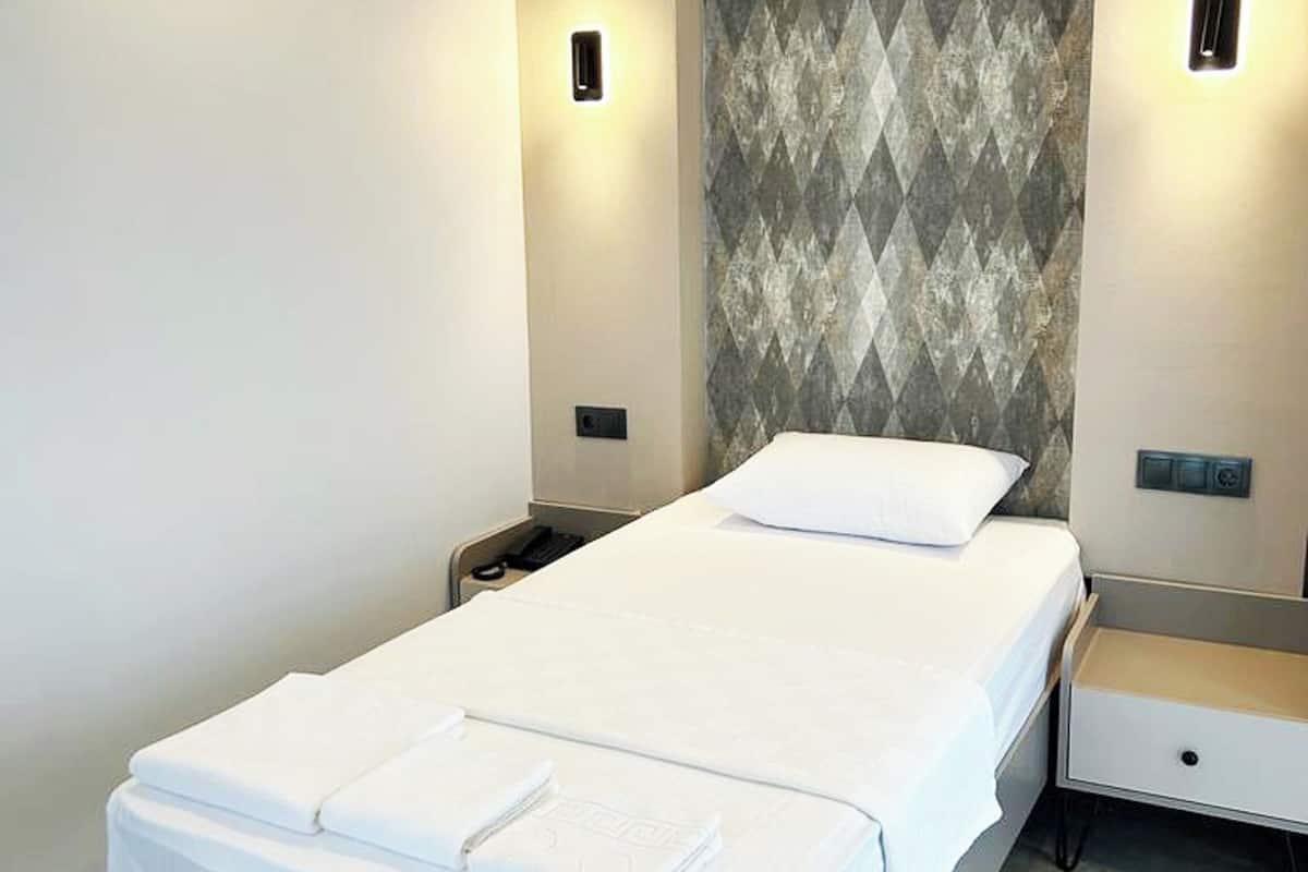 A modern hotel room with a large bed, a nightstand, a wall-mounted light, and a patterned wallpaper.