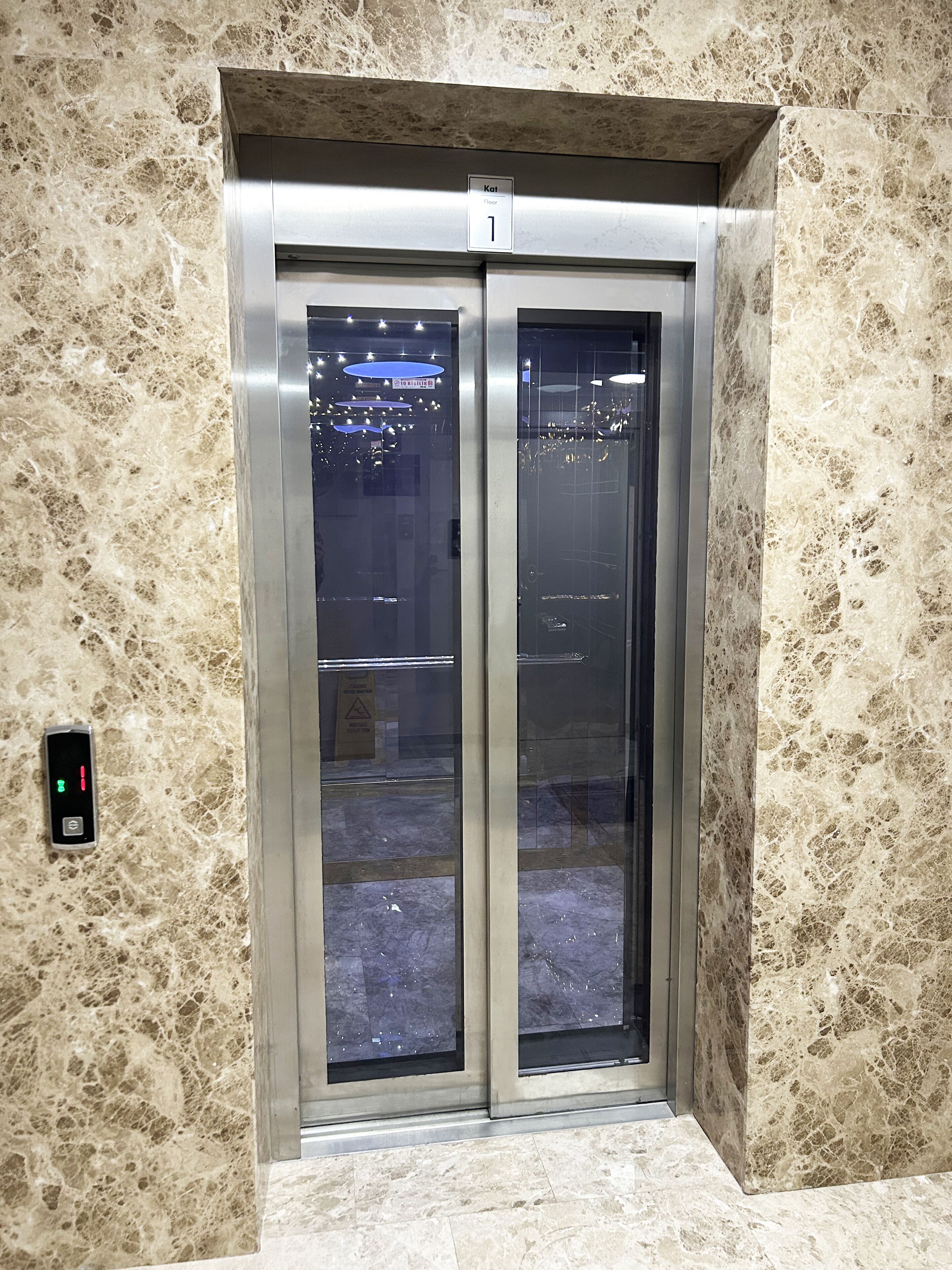 Un ascensor con pared y suelo de mármol, una pantalla digital e indicador de piso.