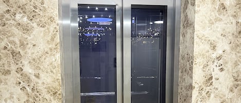 Un ascensor con pared y suelo de mármol, una pantalla digital e indicador de piso.