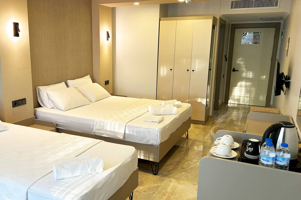 A hotel room with two beds, a minibar, and a bathroom visible in the background.