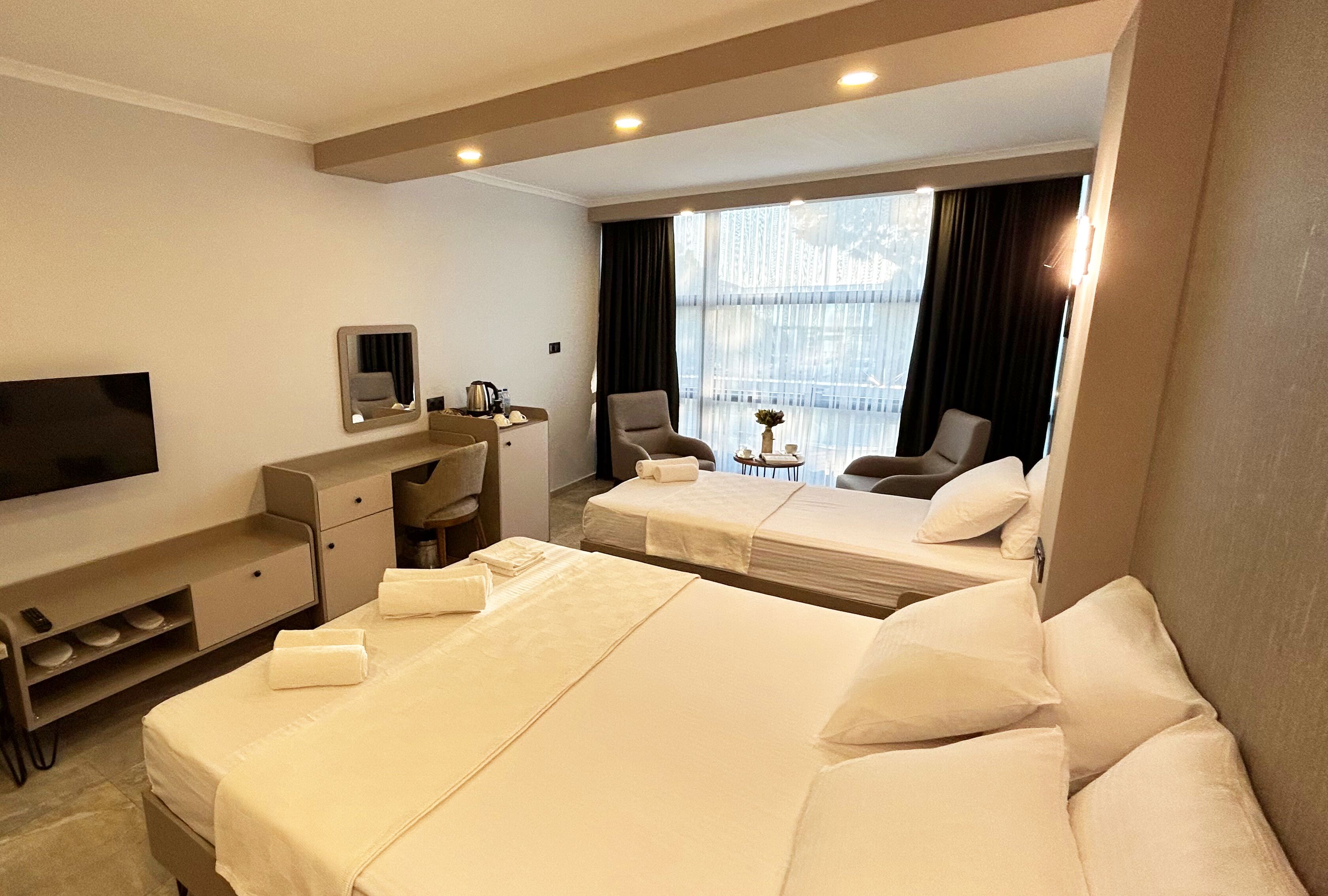 A hotel room with two beds, a TV, a desk, and a window with curtains.