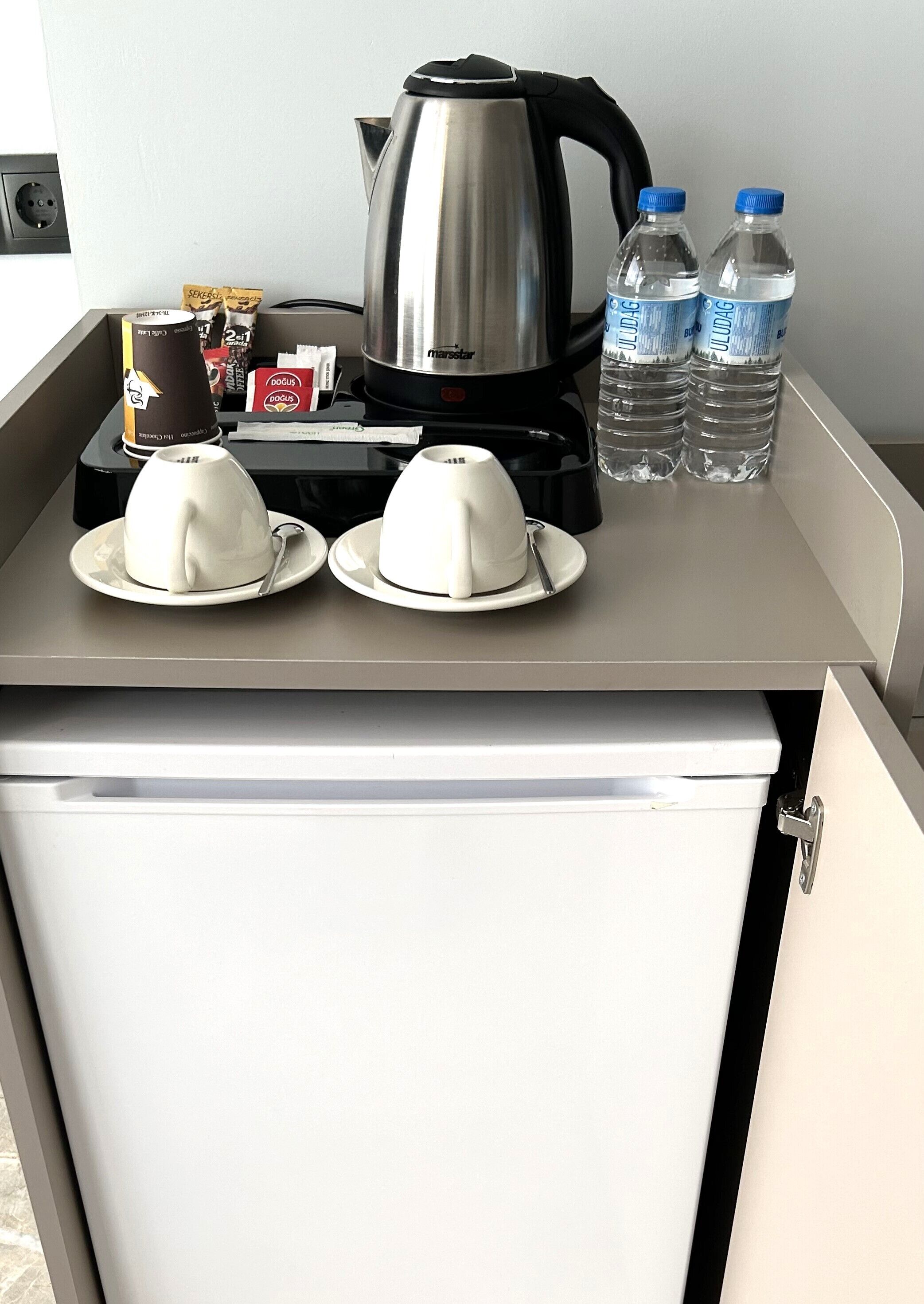 A kitchenette with a coffee maker, two cups, and two water bottles.