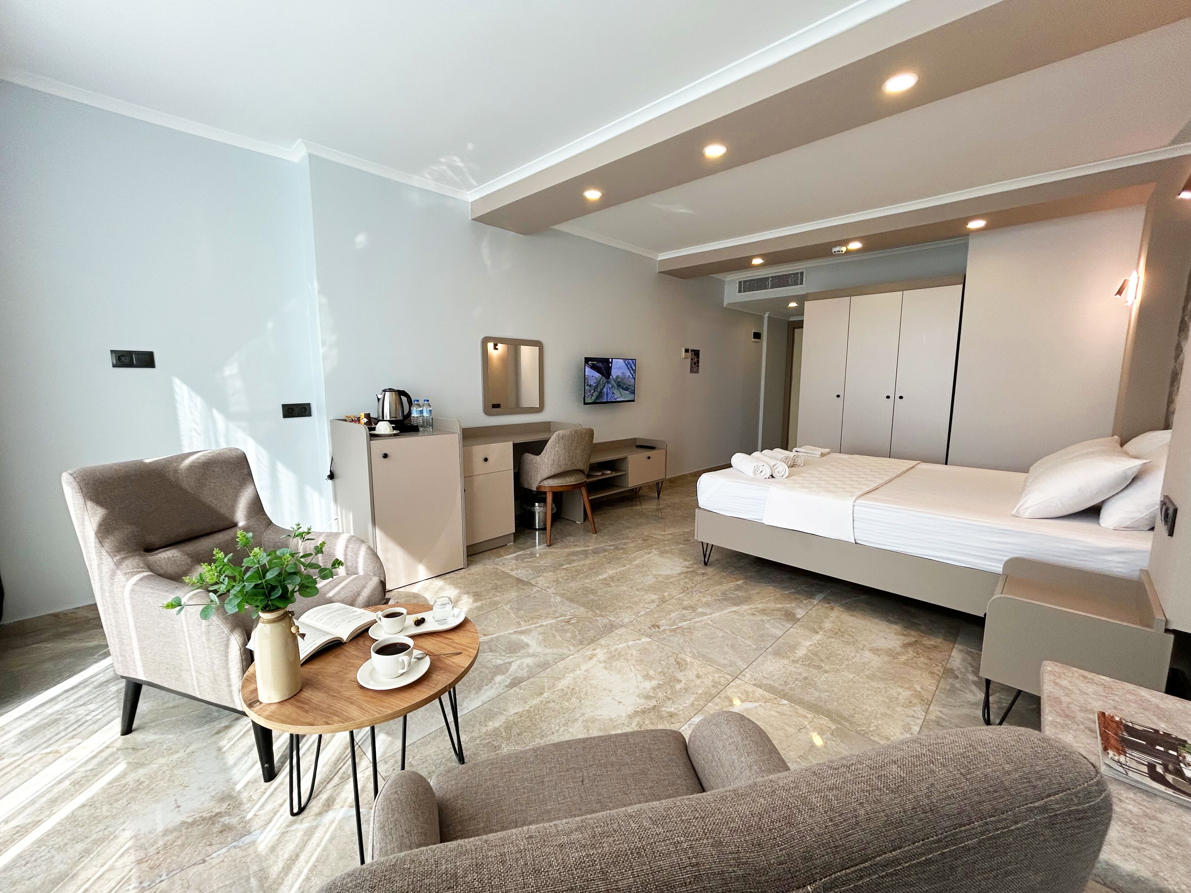 A modern hotel room with a bed, a desk, a chair, and a small seating area.