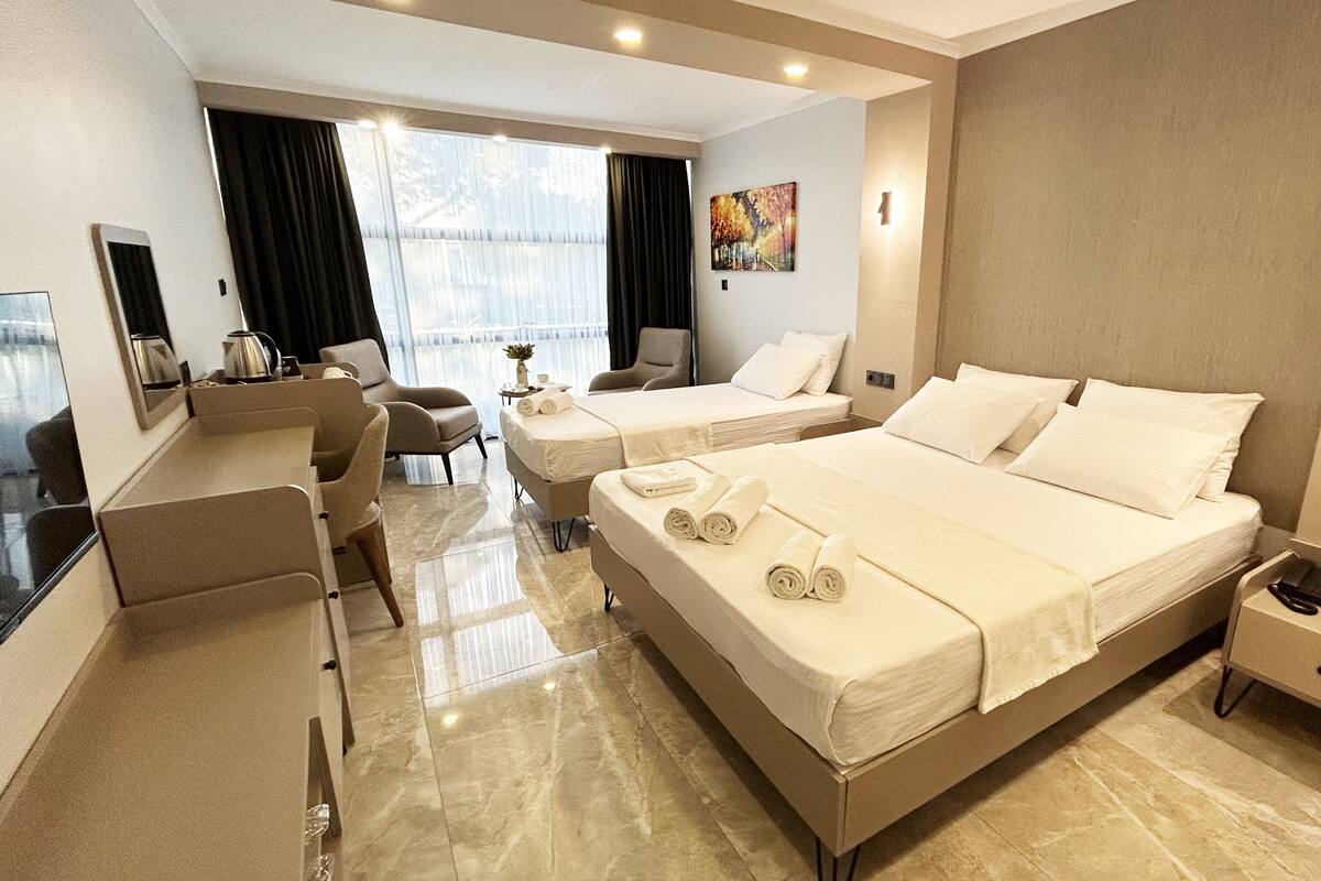 A hotel room with two beds, a desk, a chair, and a large window.