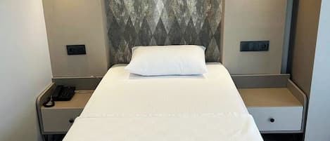 Una habitación de hotel con una cama, mesitas de noche, un teléfono y lámparas fijadas a la pared.