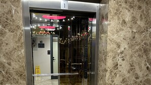 An elevator with a marble wall and floor, a sign indicating 'Floor 1', and a caution sign on the door.