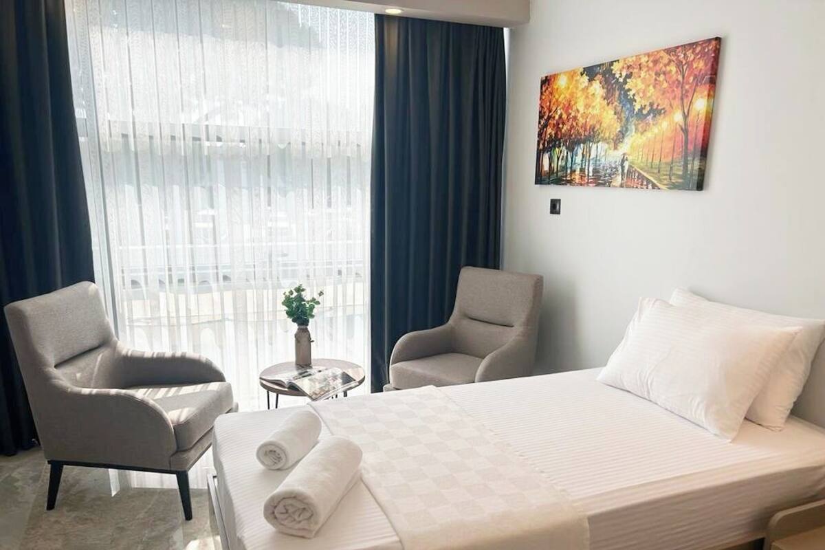 A hotel room with a bed, two armchairs, a small table with a plant, and a painting on the wall.