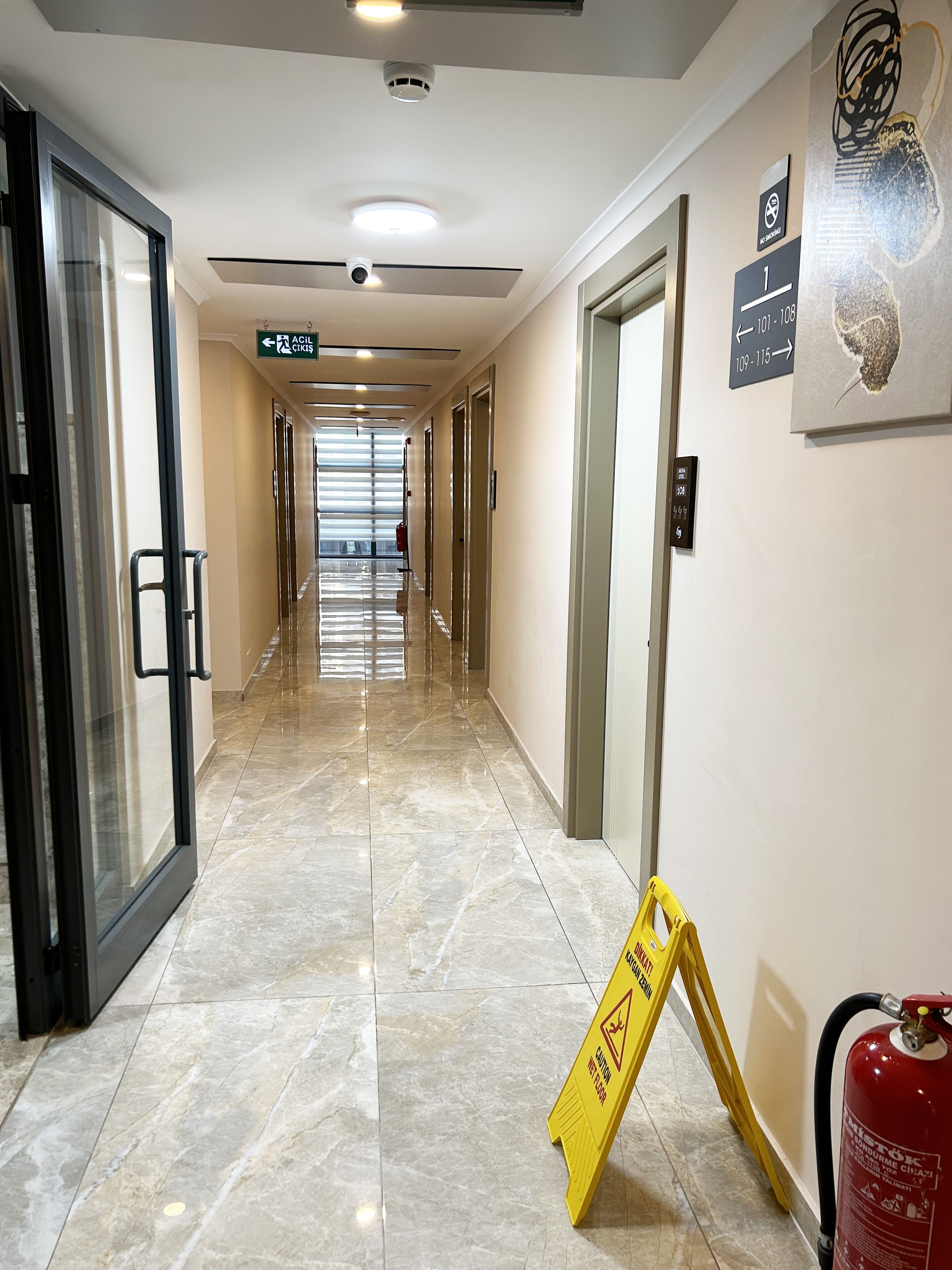Un pasillo de hotel con un extintor, un letrero de precaución y señales direccionales.