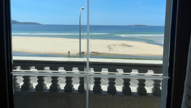 Uitzicht op een strand door een raam met een balustrade.