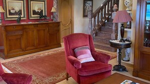 Een ruime woonkamer met een rode fauteuil, een houten salontafel en een rode bank. Achterin is een houten kast en een trap zichtbaar.