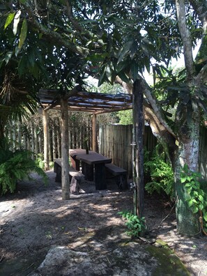 A wooden pergola with a table and benches in a garden area surrounded by trees and plants. - Deus Mim Deu (Porto Seguro)