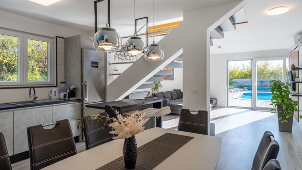 A modern kitchen with a built-in oven, a dining area with a table and chairs, and a view of a swimming pool.
