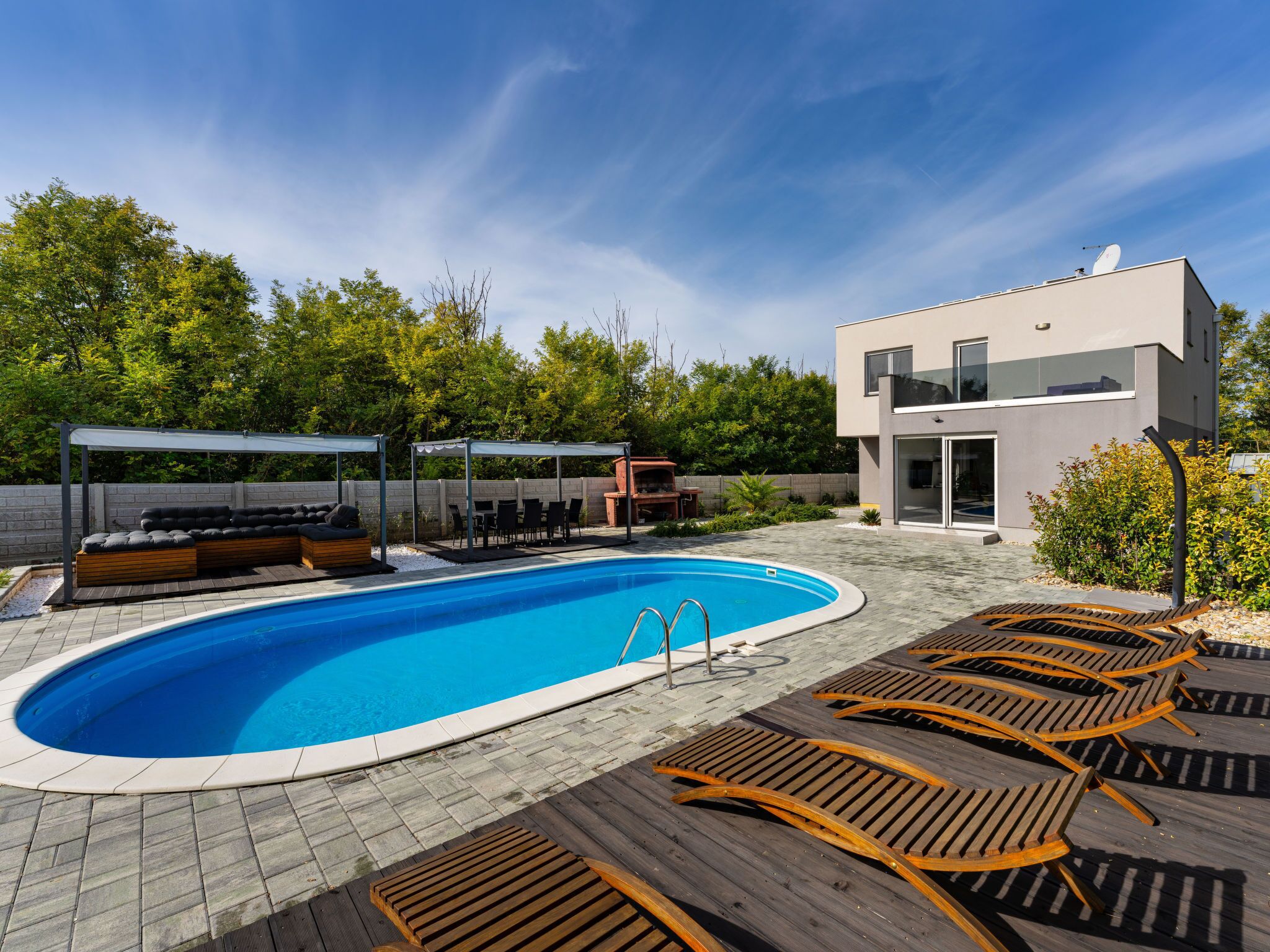 Un área de piscina moderna al aire libre con una zona de estar integrada, sillones reclinables y un edificio contemporáneo con amplias ventanas.