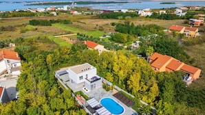 An aerial view of a residential area with modern houses, a swimming pool, and a large body of water in the background.