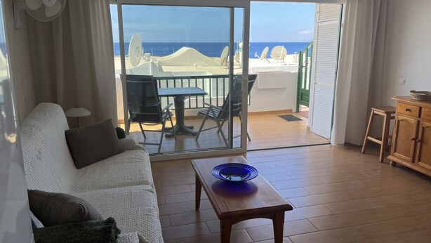A room with a sofa, a table, and a view of the sea through a sliding glass door. - Harbour Lights Puerto del Carmen (Puerto del Carmen)