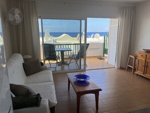 Une pièce comprenant un canapé, une table et donnant sur la mer grâce à une porte-fenêtre coulissante.