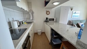 A compact kitchen with a microwave, kettle, and coffee maker on the countertop. There is a small trash bin and a stool near the sink. - Harbour Lights Puerto del Carmen (Puerto del Carmen)