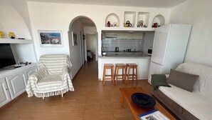 A living room with a sofa, a coffee table, and a TV. There is a kitchen area with a fridge, a sink, and a countertop. - Harbour Lights Puerto del Carmen (Puerto del Carmen)