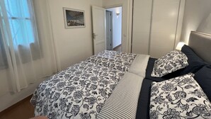 A bedroom with a bed, a nightstand, a lamp, and a door leading to another room. - Harbour Lights Puerto del Carmen (Puerto del Carmen)