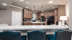 A modern kitchen with marble countertops, wooden cabinets, and a central island. There are four blue chairs around the island and a black refrigerator. - Vineyard Vista Retreat | Close to Wineries, Lakes, & More! Sleeps 6, Hot Tub (Clements)