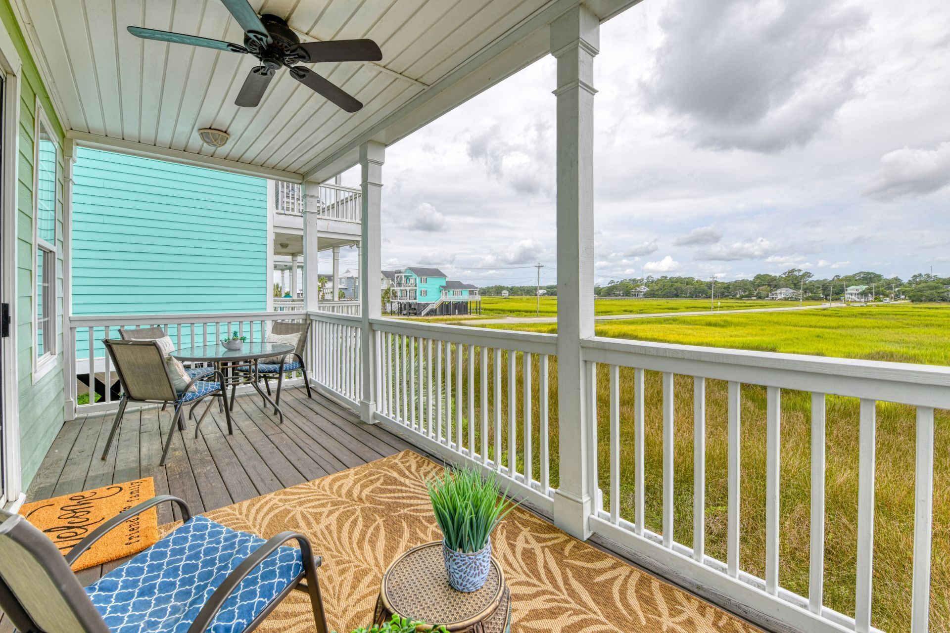 A covered porch with a table and chairs, a ceiling fan, and a view of a green field.