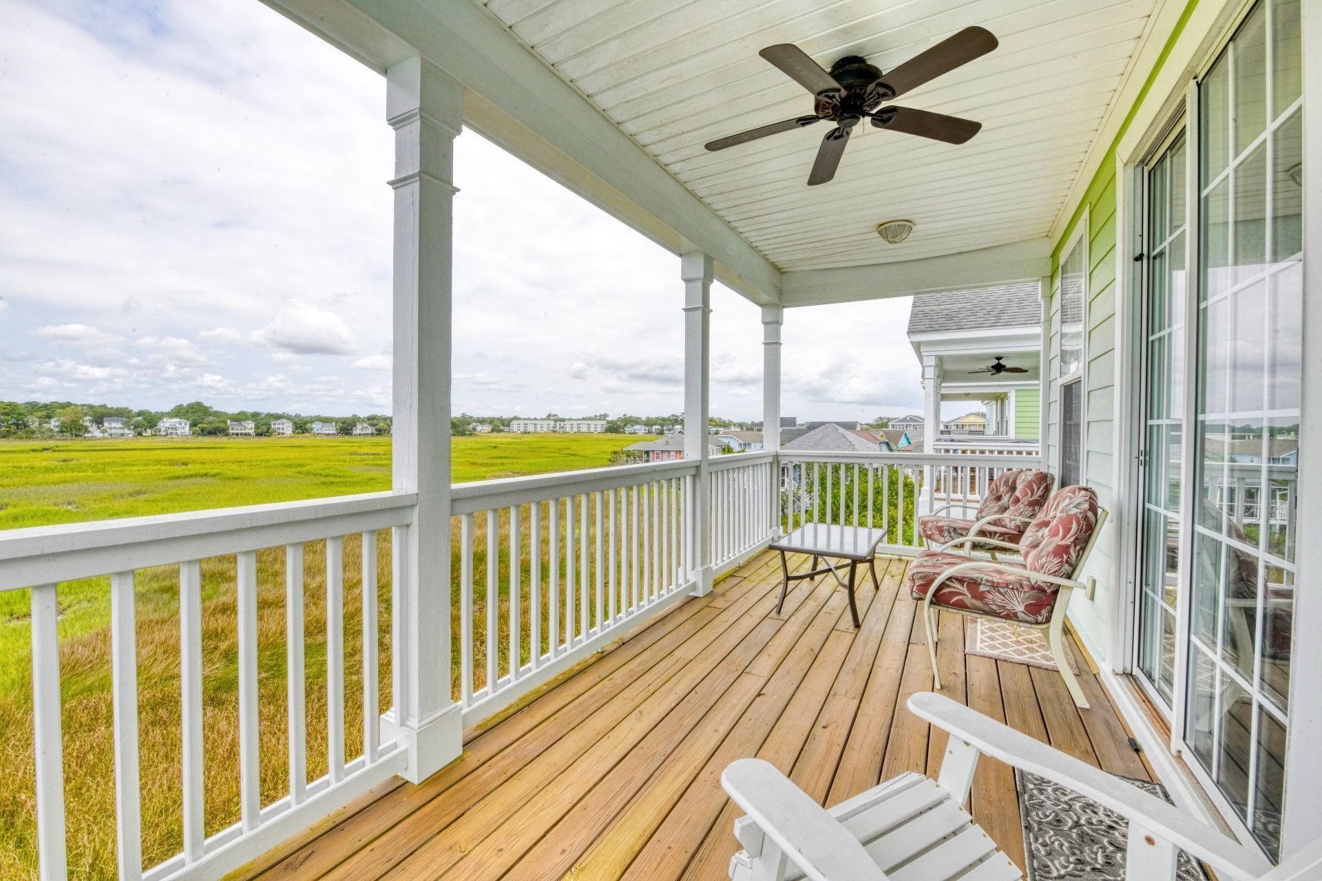 A covered porch with a wooden deck, white railings, and two Adirondack chairs.