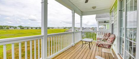 A covered porch with a wooden deck, white railings, and two Adirondack chairs.