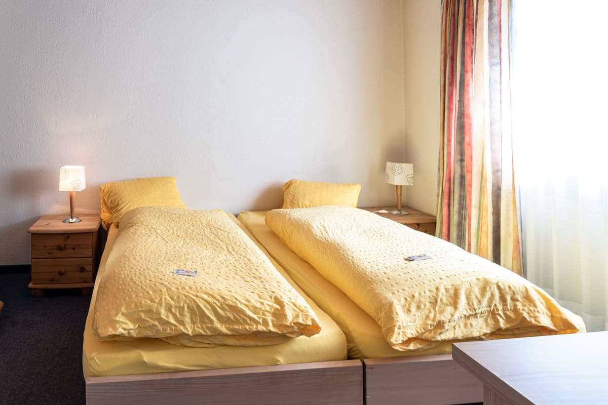Ein Doppelbett mit gelber Bettwäsche, zwei Nachttische mit Lampen und ein Fenster mit gestreiften Vorhängen.