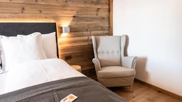 A bedroom with a wooden headboard, a bed with white bedding, a grey throw blanket, and a beige armchair.