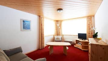 A cozy living room with a wooden ceiling, a red carpet, a sofa, a TV stand, and a table.