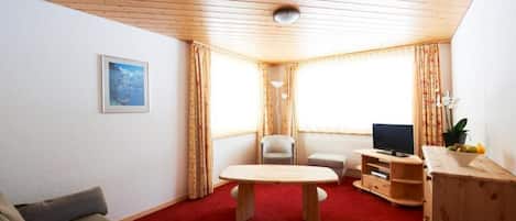 A cozy living room with a wooden ceiling, a red carpet, a sofa, a TV stand, and a table.