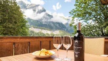 Ein Tisch mit einer Flasche Agliantino Puscia Wein, zwei leeren Weingläsern und einer Chipsplatte, vor einer Bergkulisse.