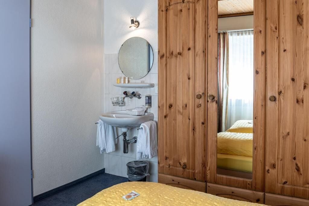 Una habitación de hotel con un armario de madera, un lavabo con espejo y una cama con colcha amarilla.