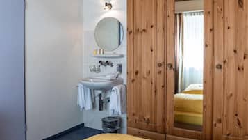 Una habitación de hotel con un armario de madera, un lavabo con espejo y una cama con colcha amarilla.