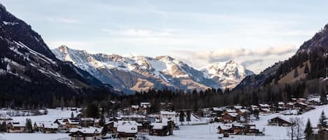 A snow-covered village with traditional wooden houses, a ski slope, and a mountain range in the background.