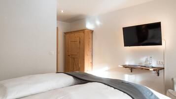 A bedroom with a bed, a wooden wardrobe, a mounted TV, and a shelf with bottles.
