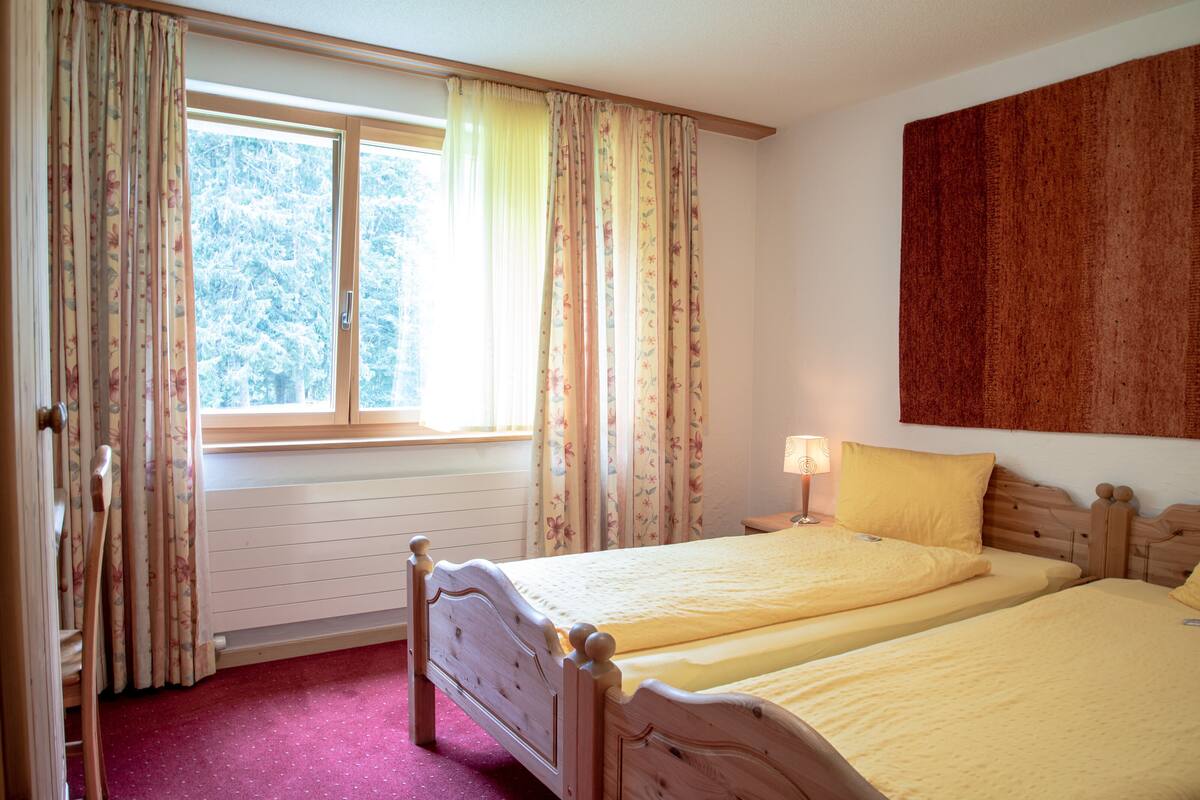 Ein Schlafzimmer mit zwei Betten, einem Fenster mit Vorhängen, einem Heizkörper und einem Wandbild.
