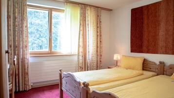 A bedroom with two beds, a window with curtains, a radiator, and a wall-mounted artwork.