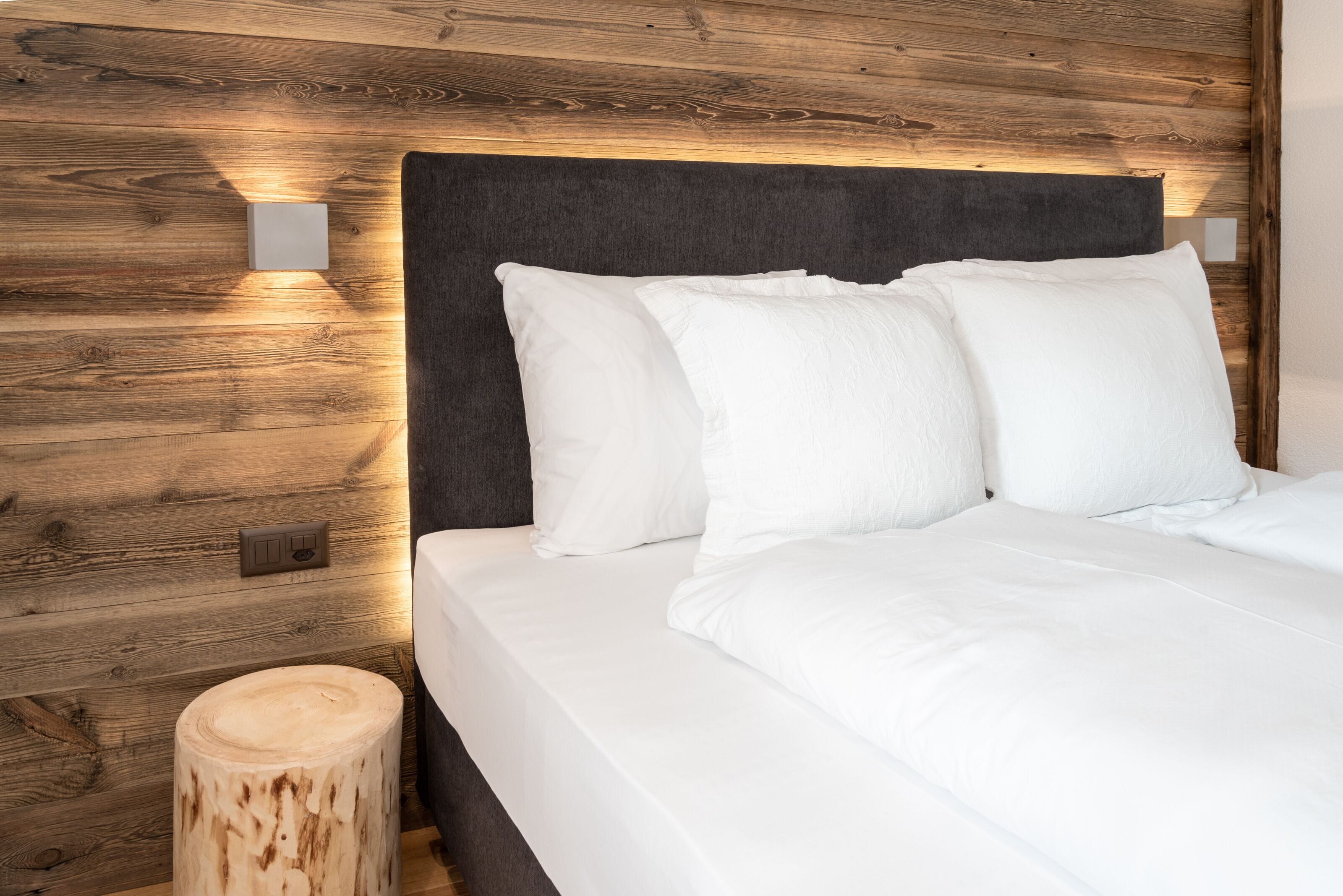 A neatly made bed with white linens and pillows, a dark headboard, and wooden wall paneling.