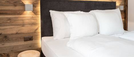 A neatly made bed with white linens and pillows, a dark headboard, and wooden wall paneling.