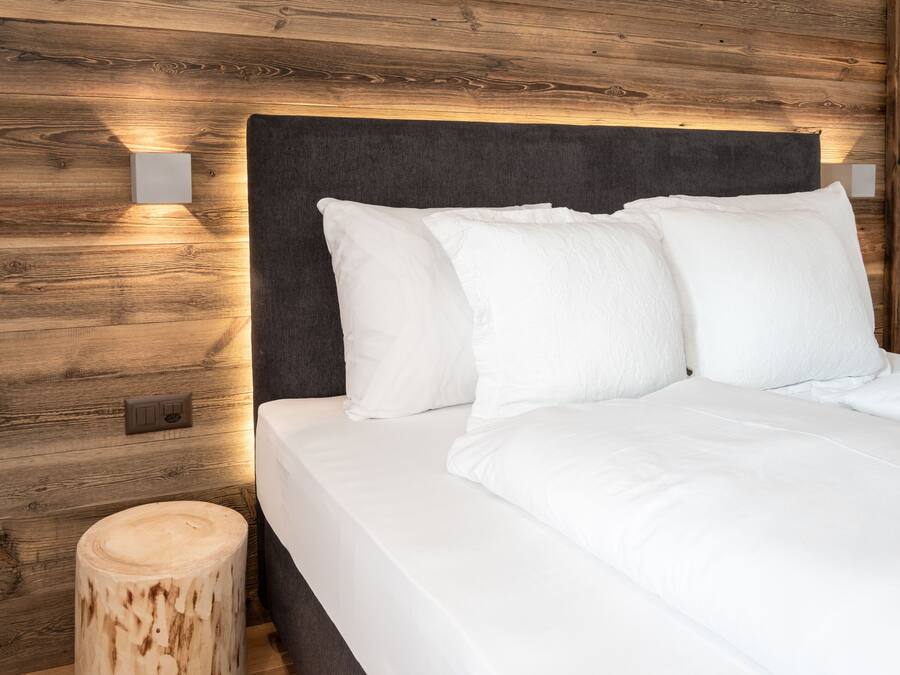 Un lit bien fait, avec du linge de lit blanc et des oreillers, une tête de lit sombre et un lambris en bois.